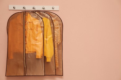 Photo of Garment bags with clothes hanging on light wall. Space for text