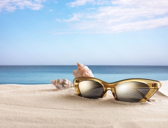Image of Shells and stylish sunglasses on sandy beach near sea