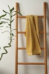 Photo of Yellow towel on wooden ladder and houseplant indoors