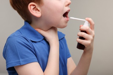 Photo of Little boy using throat spray on grey background, closeup
