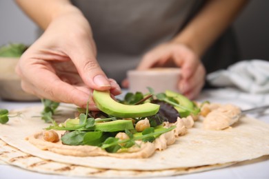 Woman making delicious hummus wrap with vegetables at table, closeup
