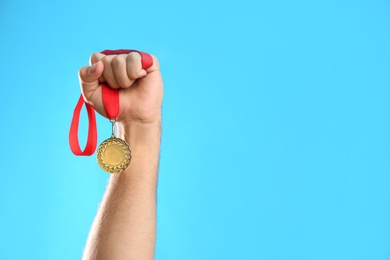 Photo of Man holding golden medal on light blue background, closeup. Space for design