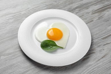 Plate with heart shaped fried egg on white wooden table