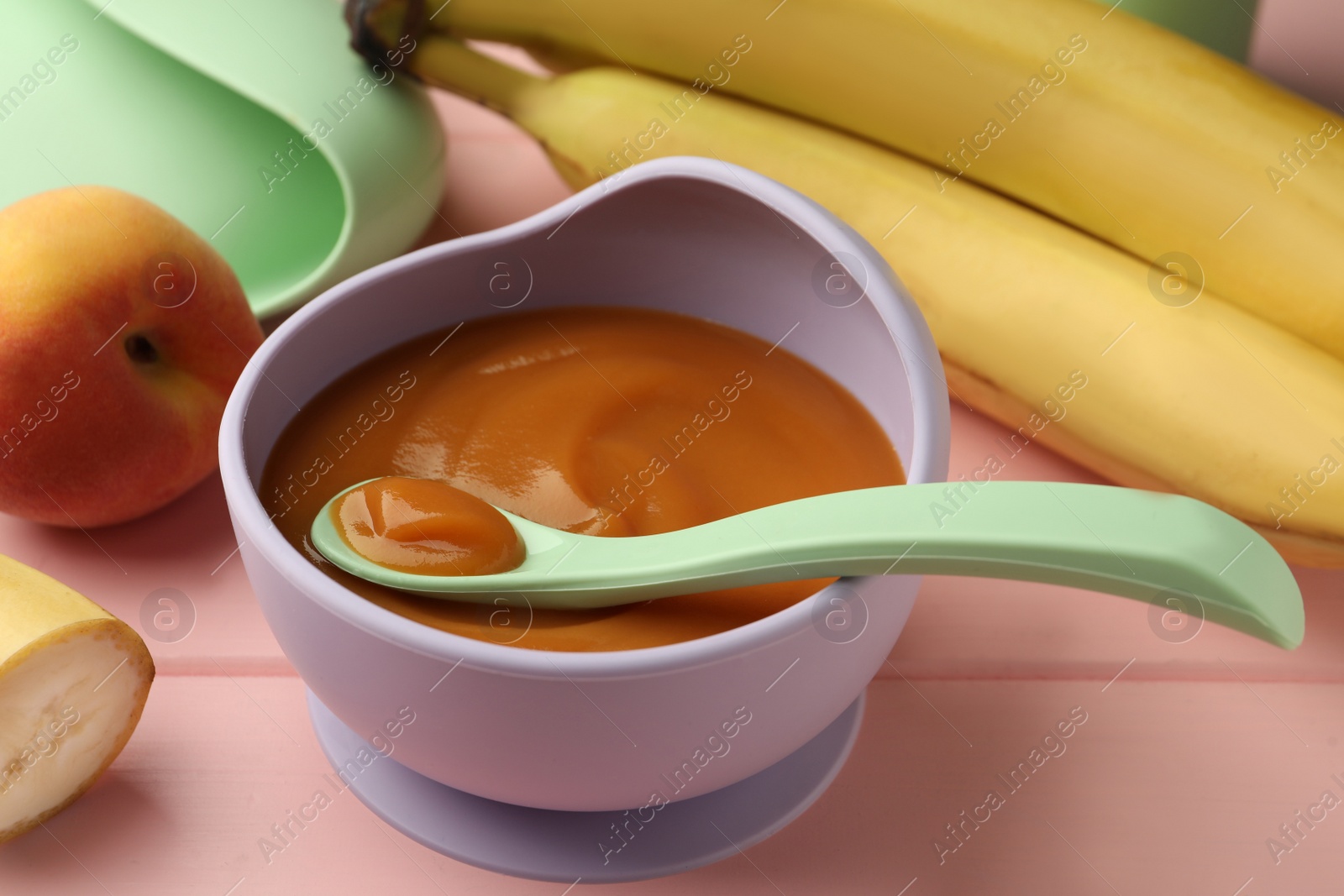 Photo of Healthy baby food in bowl and fresh fruits on pink wooden table, closeup