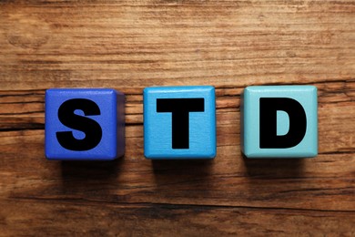 Photo of Colorful cubes with letters STD (sexually transmitted diseases) on wooden table, flat lay