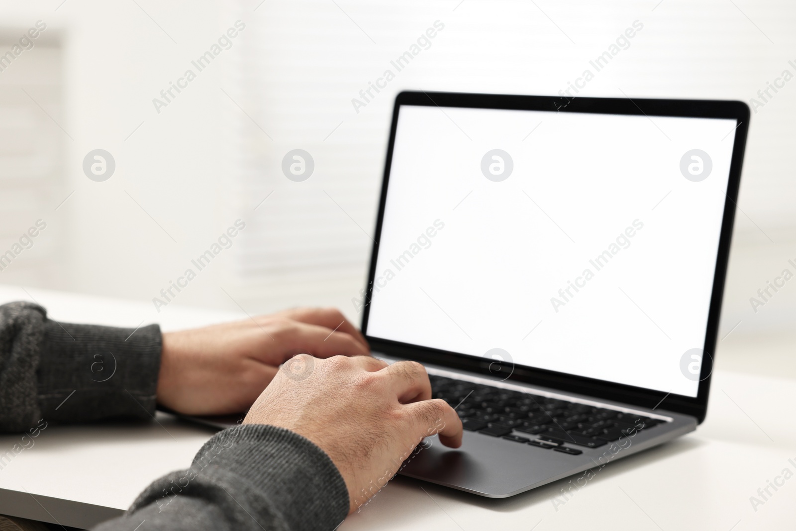 Photo of E-learning. Young man using laptop at white table indoors, closeup