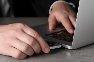 Photo of Man connecting usb flash drive to laptop at grey table, closeup