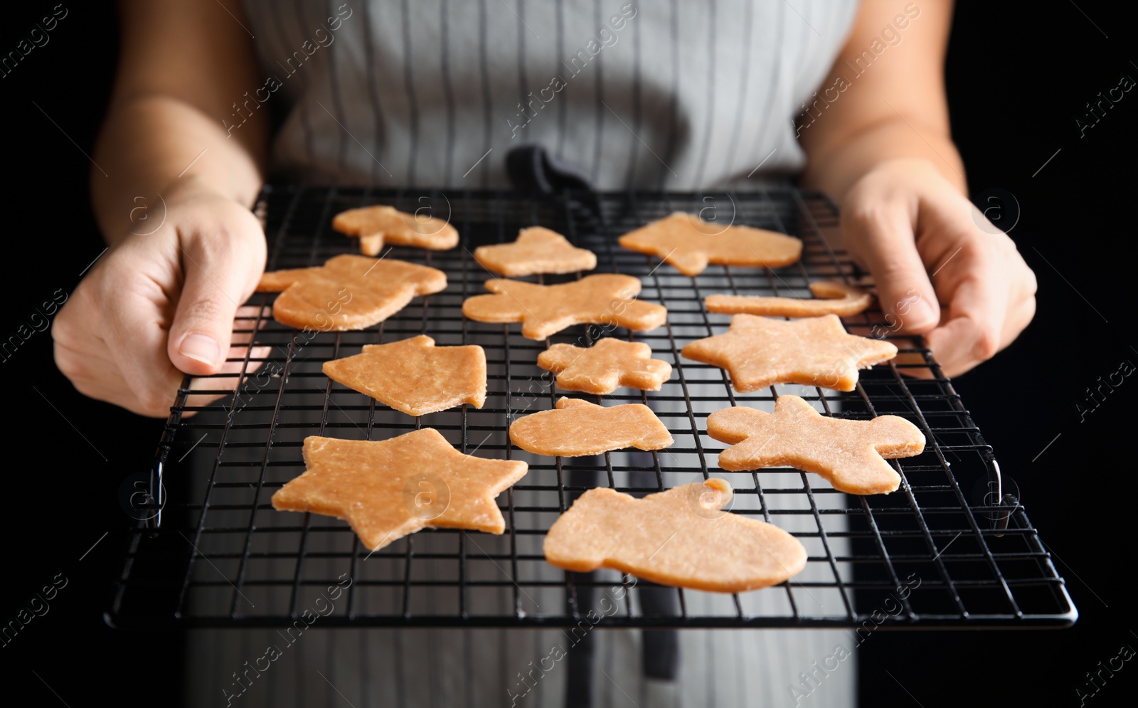 Photo of Woman holding baking grid with unbaked Christmas cookies on black background, closeup