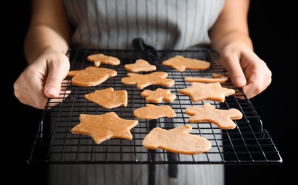 Woman holding baking grid with unbaked Christmas cookies on black background, closeup