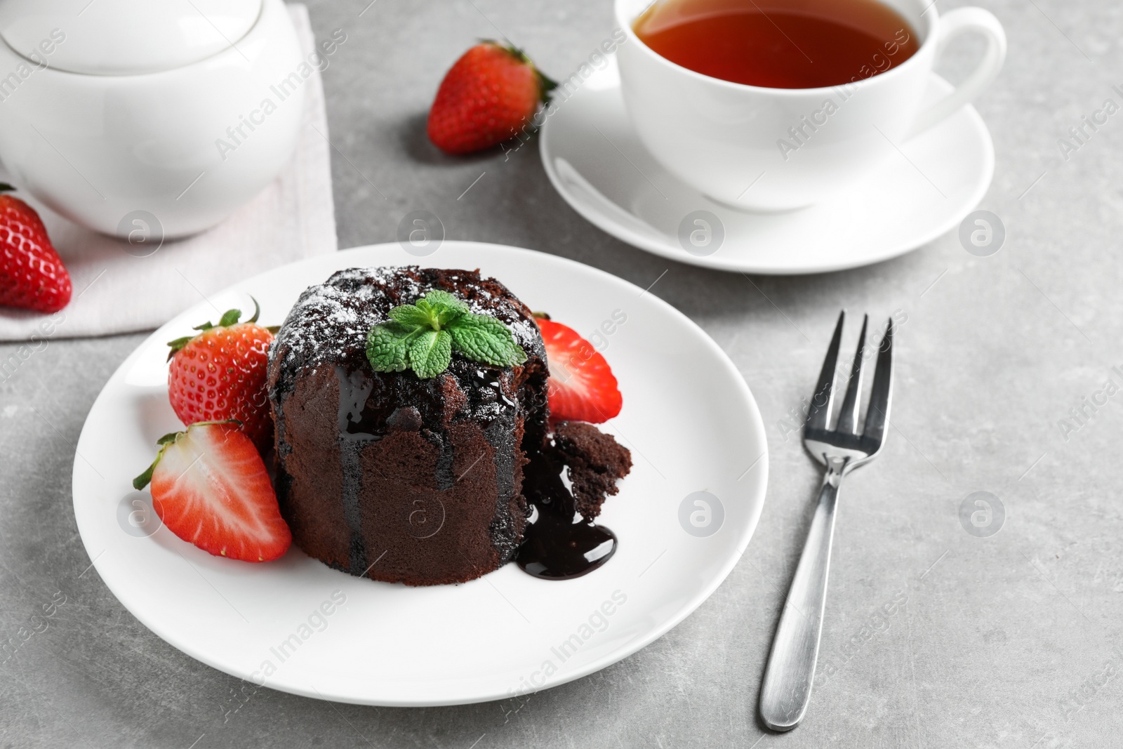 Photo of Delicious warm chocolate lava cake with mint and strawberries on table