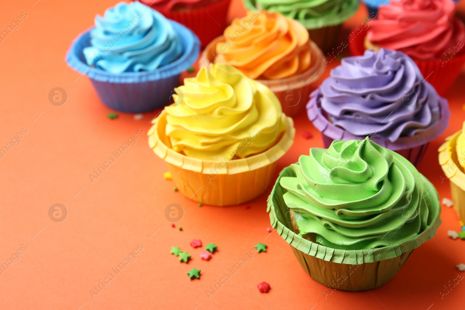 Photo of Delicious bright cupcakes and sprinkles on coral background, closeup