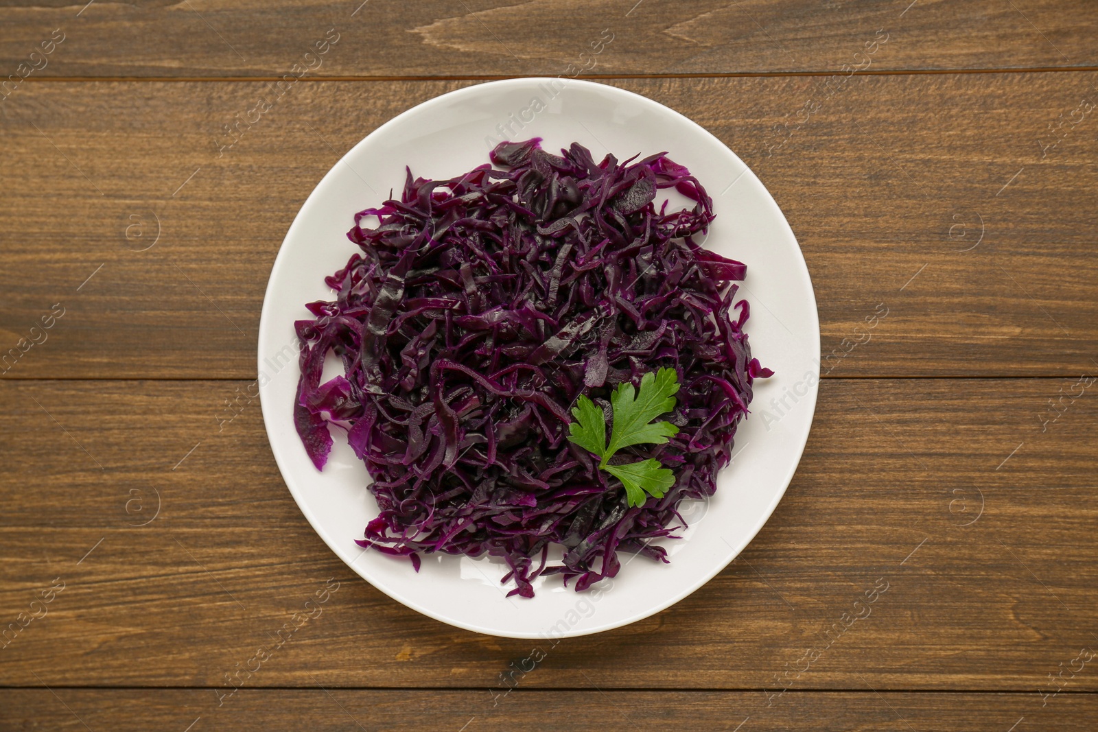 Photo of Tasty red cabbage sauerkraut with parsley on wooden table, top view