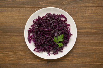 Photo of Tasty red cabbage sauerkraut with parsley on wooden table, top view