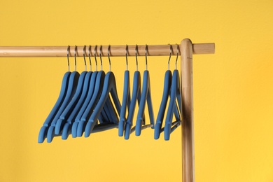 Wooden rack with clothes hangers on color background