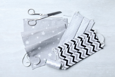 Photo of Homemade protective masks and sewing accessories on light background, flat lay