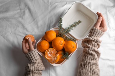Woman with delicious ripe tangerines on white bedsheet, top view