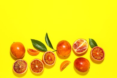 Photo of Many ripe sicilian oranges and leaves on yellow background, flat lay. Space for text
