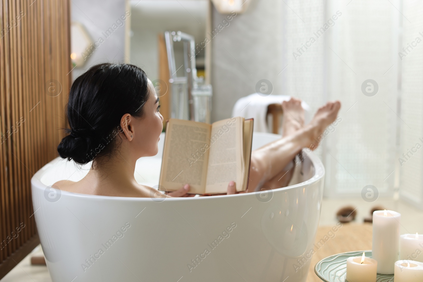 Photo of Beautiful young woman reading book while taking bath at home