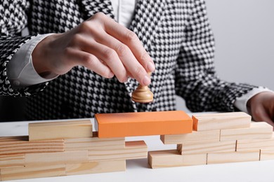 Photo of Businesswoman putting white pawn on bridge made of wooden blocks at table, closeup. Connection, relationships and deal concept