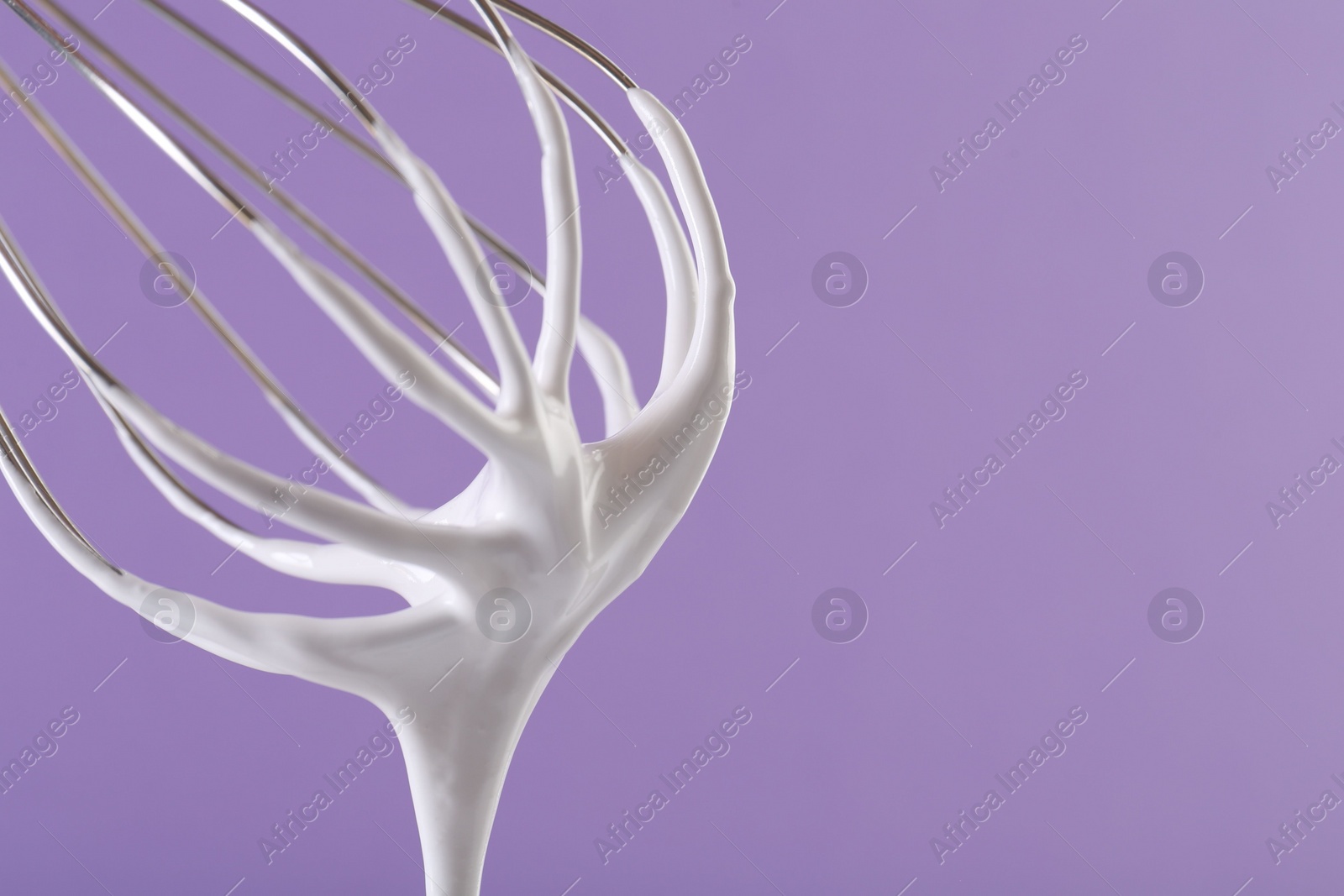 Photo of Whisk with whipped cream on violet background, closeup. Space for text