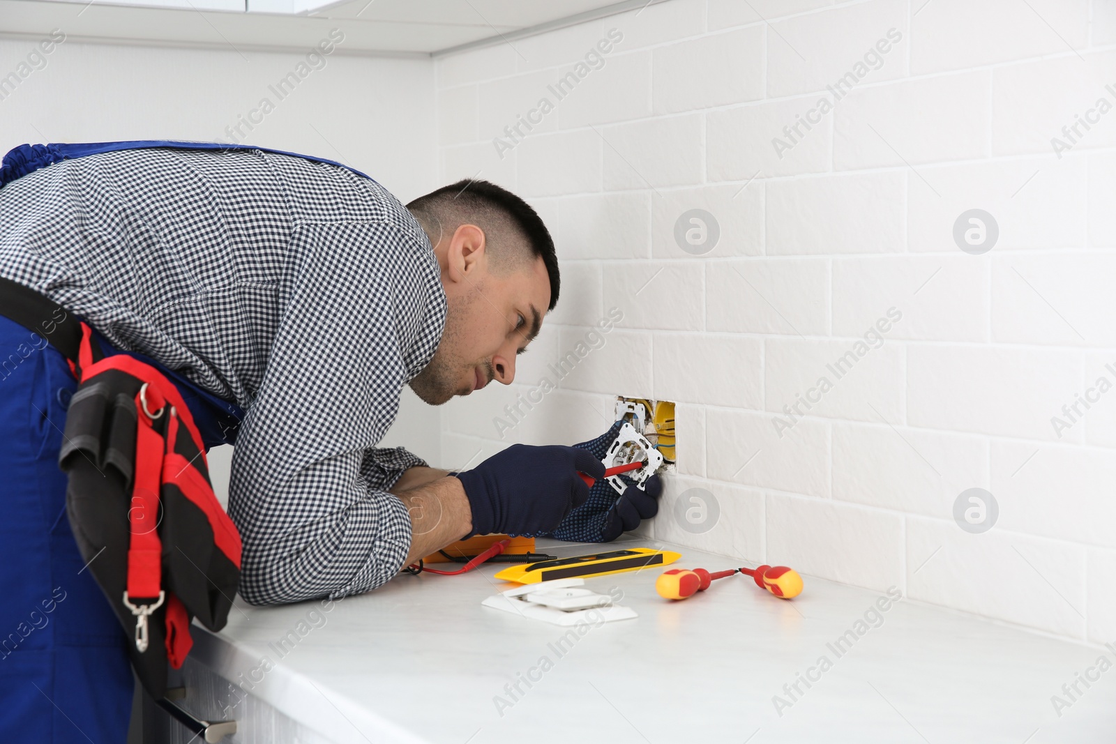 Photo of Electrician with screwdriver repairing power socket indoors