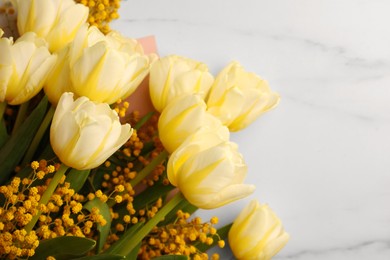 Bouquet with beautiful tulips and mimosa flowers on white marble table, top view. Space for text