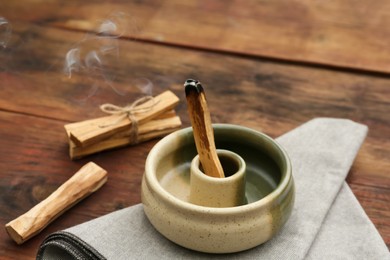 Palo Santo stick smoldering in holder on wooden table