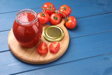 Photo of Organic ketchup in jar and fresh tomatoes on blue wooden table, space for text. Tomato sauce