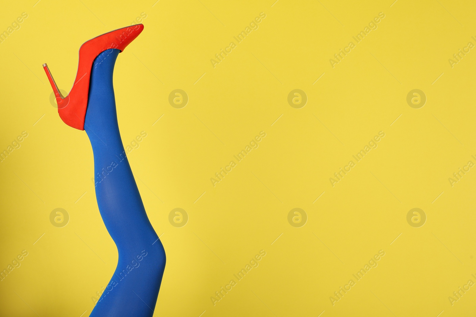 Photo of Woman wearing blue tights and high heel shoe on yellow background, closeup. Space for text