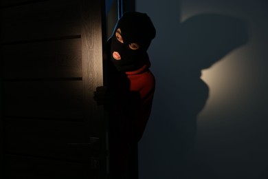 Thief in balaclava entering foreign house at night, space for text. Burglary