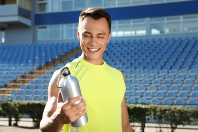 Sporty man with bottle of water at stadium on sunny day