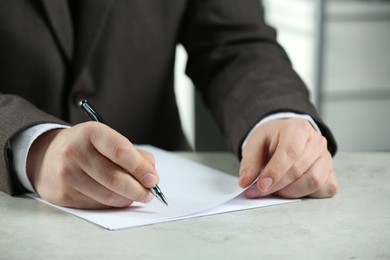 Photo of Man writing on sheet of paper with pen at white table, closeup