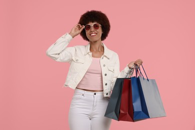 Photo of Happy young woman in stylish sunglasses with shopping bags on pink background