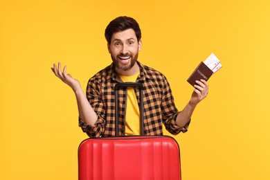 Smiling man with passport, tickets and suitcase on yellow background