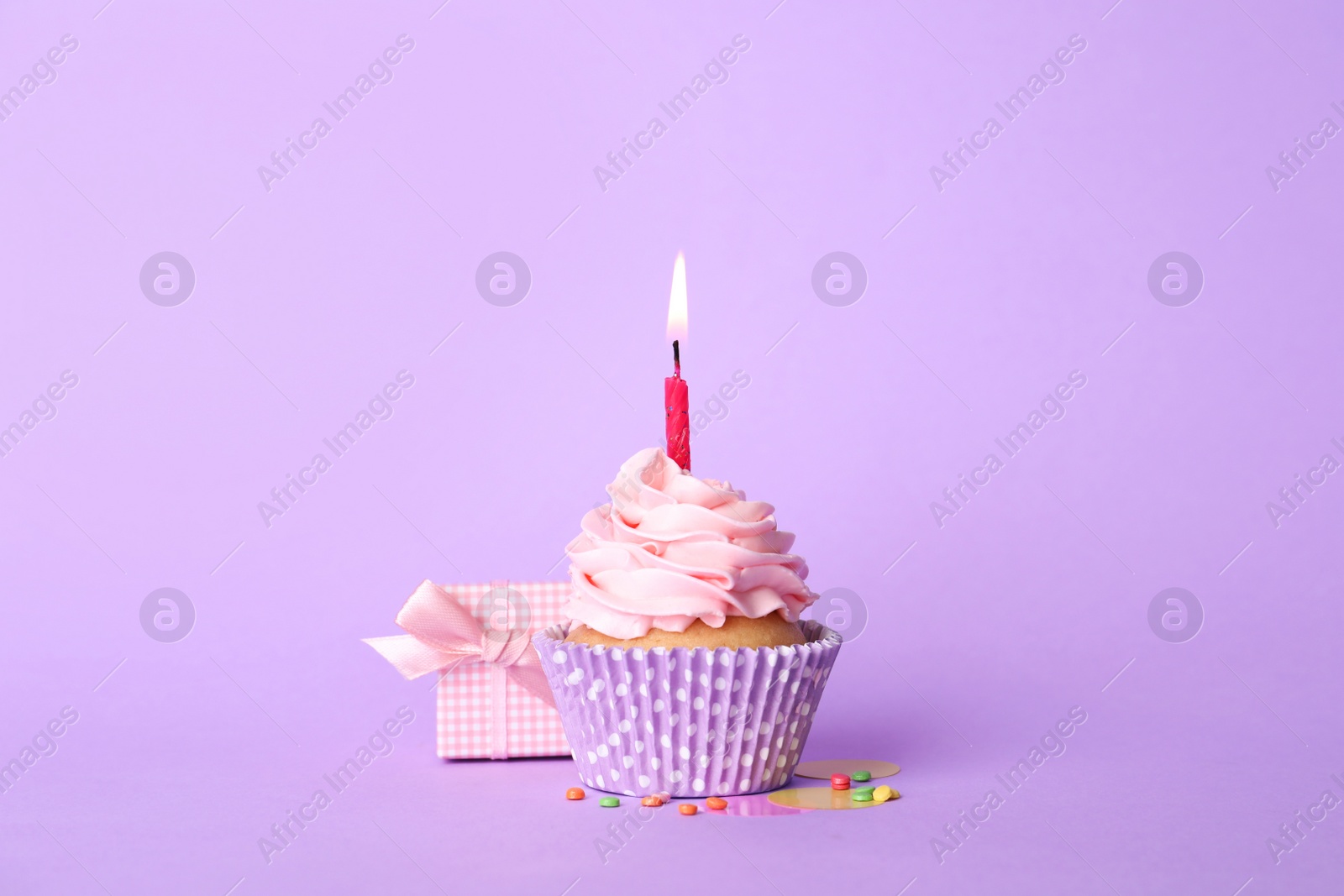Photo of Birthday cupcake with burning candle and gift box on violet background