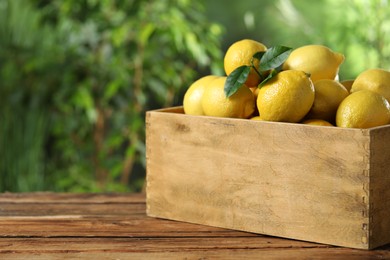 Fresh lemons in crate on wooden table. Space for text