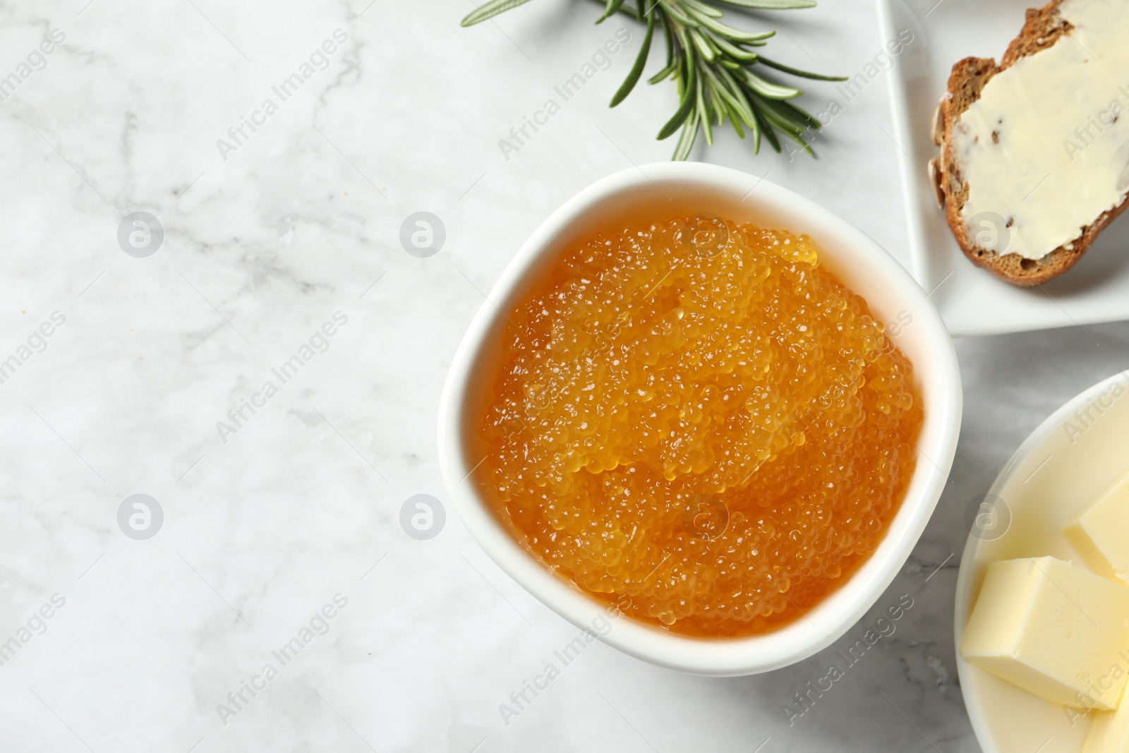 Photo of Fresh pike caviar in bowl, bread, rosemary and butter on white marble table, flat lay. Space for text