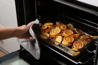 Photo of Woman taking delicious lemon chicken out of oven, closeup