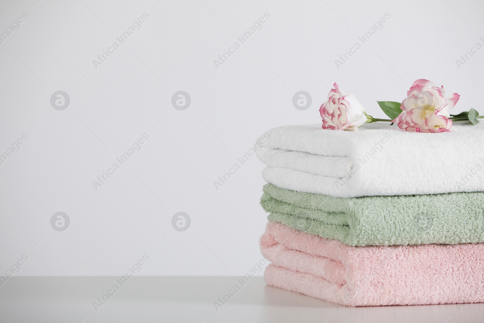 Photo of Soft folded towels with eustoma flowers on white table, space for text