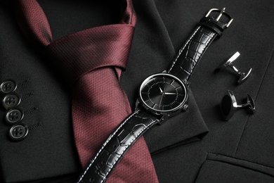 Photo of Luxury wrist watch, tie and cufflinks on black jacket, closeup