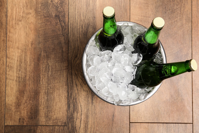 Beer in metal bucket with ice on wooden background, top view. Space for text