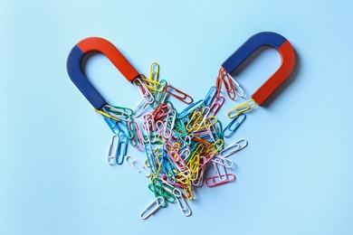 Photo of Red and blue horseshoe magnets attracting colorful paperclips on light blue background, flat lay