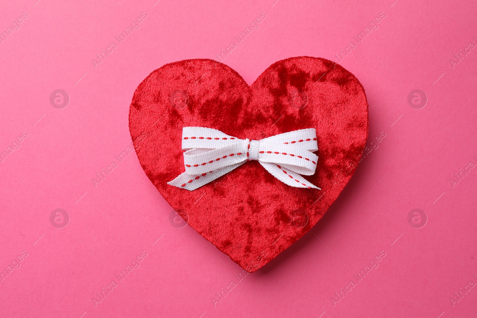 Photo of Red textile heart with white bow on pink background, top view