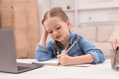 Photo of Little girl suffering from headache while doing homework at home