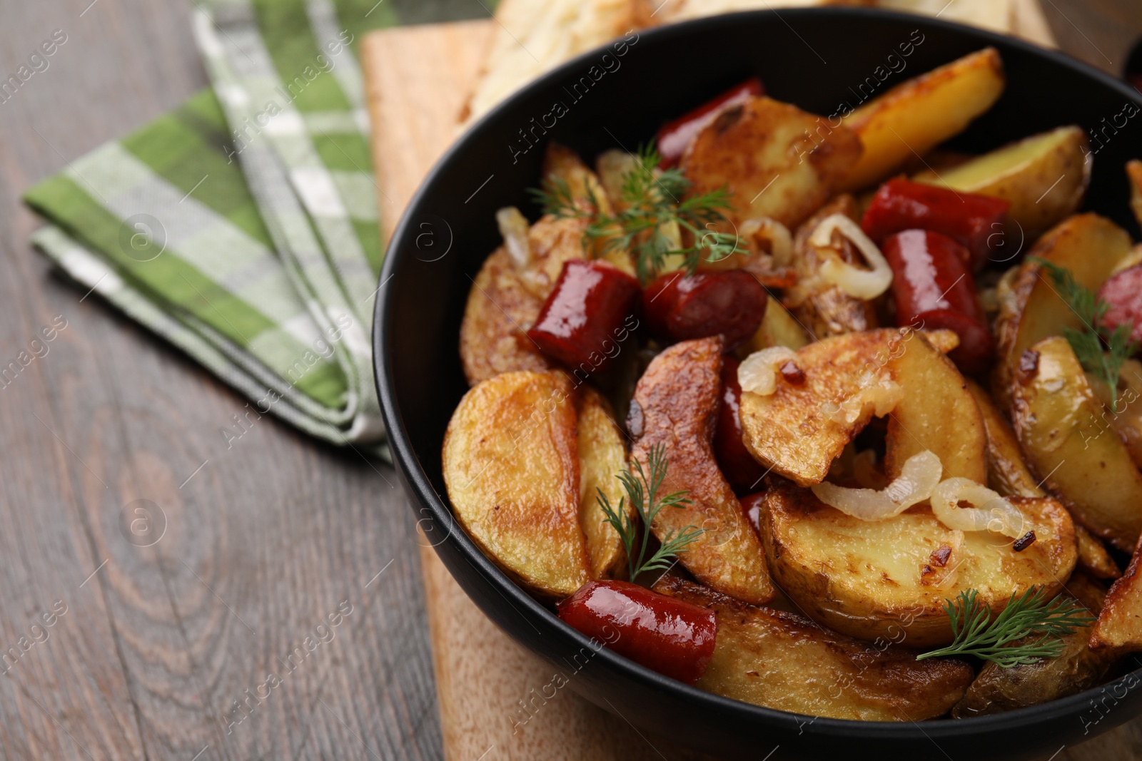 Photo of Delicious baked potato with thin dry smoked sausages, onion and dill in bowl on wooden table, closeup. Space for text