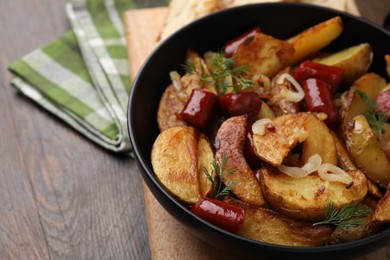 Photo of Delicious baked potato with thin dry smoked sausages, onion and dill in bowl on wooden table, closeup. Space for text