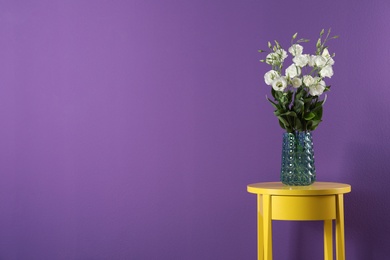 Photo of Elegant vase with eustoma flowers on table near purple wall. Space for text