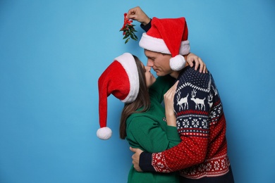 Photo of Happy couple standing under mistletoe bunch on light blue background