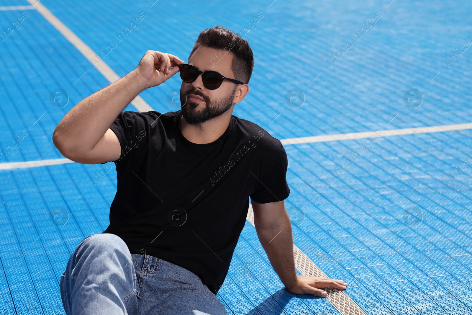 Photo of Handsome man in sunglasses on blue floor covering outdoors, space for text