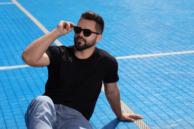 Handsome man in sunglasses on blue floor covering outdoors, space for text